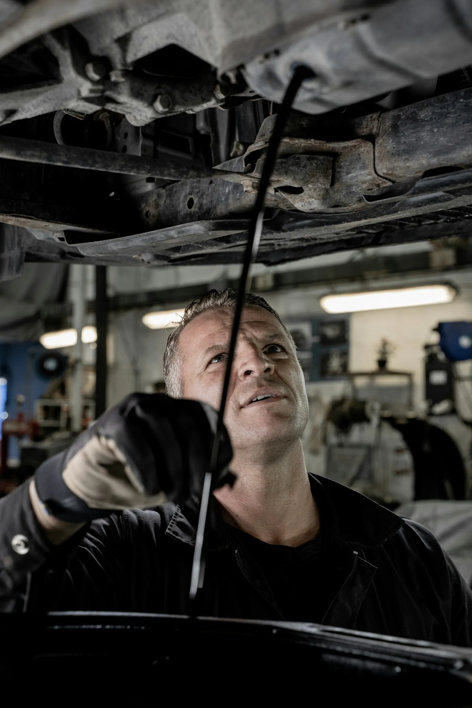 Automechanik kontroluje v dílně měrkou hladinu oleje